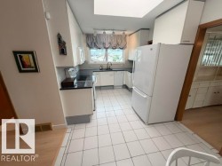Galley-style kitchen featuring white cabinetry, black countertops, a white tile backsplash, and a skylight - 