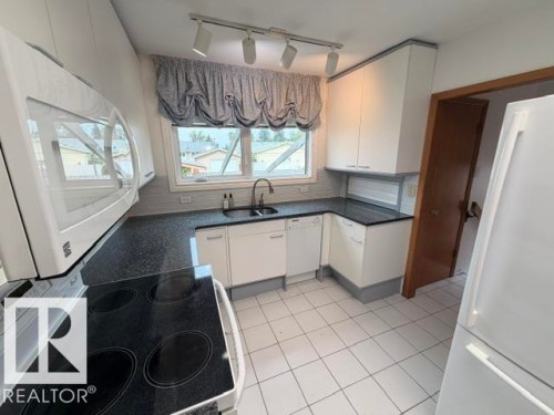 Kitchen featuring white cabinetry, dark countertops, and a white tile floor - 6824 89 Avenue Nw, Edmonton, AB - Indoor Photo Showing Kitchen With Double Sink