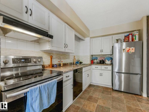 Kitchen featuring white cabinetry, stone-finish countertops, tile flooring, stainless steel appliances, and a tile backsplash - 13405 40 St Nw, Edmonton, AB - Indoor Photo Showing Kitchen