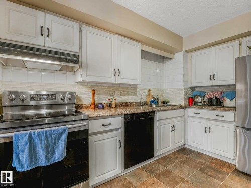 Kitchen featuring white shaker-style cabinetry, a stainless steel range, and a tile backsplash - 13405 40 St Nw, Edmonton, AB - Indoor Photo Showing Kitchen
