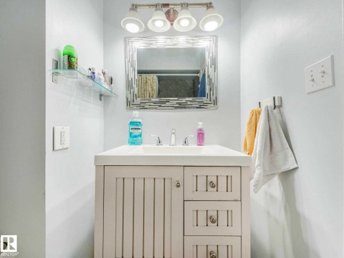 White vanity with integrated sink, mosaic-framed mirror, and a four-light fixture - 13405 40 St Nw, Edmonton, AB - Indoor