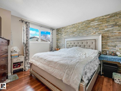 Bedroom featuring wood-finish flooring, a decorative accent wall with stacked stone, and a window providing natural light - 13405 40 St Nw, Edmonton, AB - Indoor Photo Showing Bedroom