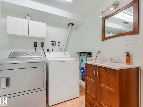 Laundry area featuring white cabinetry, a wood-finish vanity with an integrated sink, a framed mirror, and track lighting - 13405 40 St Nw, Edmonton, AB - Indoor Photo Showing Laundry Room