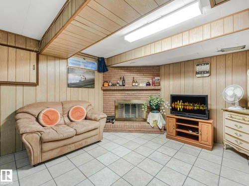 Recreational space featuring a brick fireplace, light-toned wall paneling, and white square tile flooring - 13405 40 St Nw, Edmonton, AB - Indoor With Fireplace