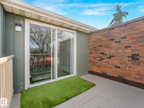 Patio area featuring a sliding glass door, brick wall, vinyl siding, and a white railing - 13405 40 St Nw, Edmonton, AB - Outdoor With Exterior