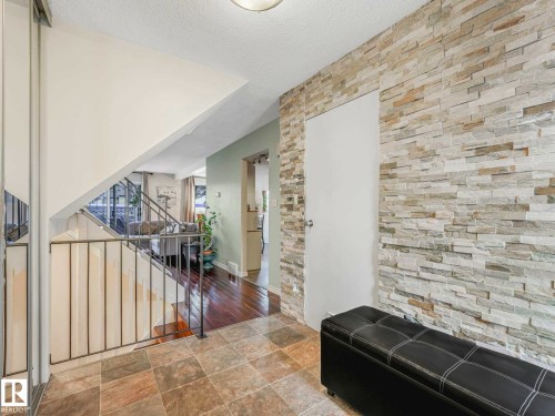 Foyer featuring a stacked stone accent wall, tile flooring, and a staircase with metal railing - 13405 40 St Nw, Edmonton, AB - Indoor Photo Showing Other Room