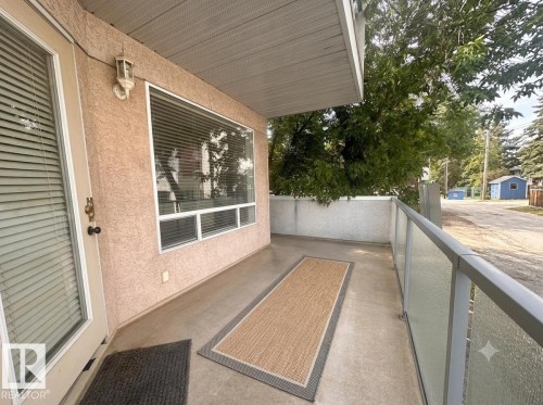 Private balcony featuring a glass panel railing, concrete flooring, and an exterior wall light - #103 8108 109 St Nw, Edmonton, AB 