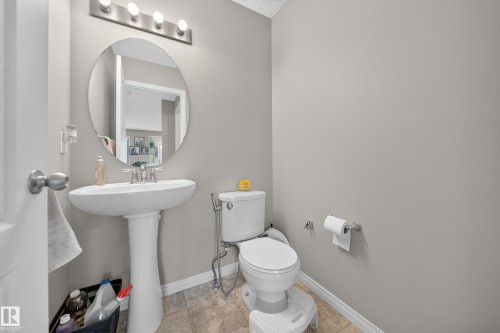 Pedestal sink with chrome fixtures, round mirror, overhead vanity lighting, and light gray wall finish - 1927 51 Street Sw, Edmonton, AB - Indoor Photo Showing Bathroom