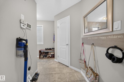 Neutral wall paint, tiled flooring, white interior door, wall-mounted mirror with a decorative frame, and a window with white louvered blinds - 1927 51 Street Sw, Edmonton, AB - Indoor Photo Showing Other Room