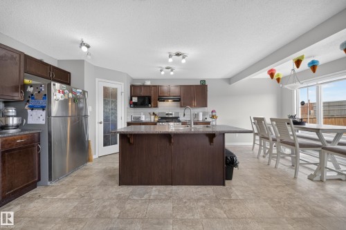 Spacious kitchen island with seating, dark wood-finish cabinetry, stainless steel appliances, and large windows providing abundant natural light - 1927 51 Street Sw, Edmonton, AB - Indoor Photo Showing Kitchen
