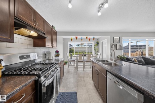 Kitchen featuring dark wood-finish cabinetry, stainless steel appliances, a subway tile backsplash, and a double basin sink - 1927 51 Street Sw, Edmonton, AB - Indoor Photo Showing Kitchen With Stainless Steel Kitchen With Double Sink