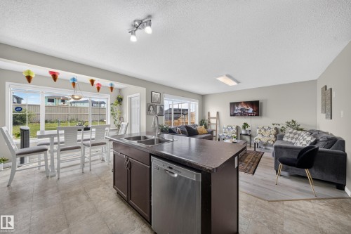 Open concept living area featuring a kitchen island with integrated sink and dishwasher, vinyl plank flooring, and a dining area with a bay window - 1927 51 Street Sw, Edmonton, AB - Indoor Photo Showing Kitchen With Double Sink