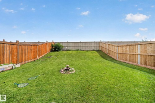 Expansive backyard featuring a green lawn, wood privacy fencing, and a built-in stone fire pit - 1927 51 Street Sw, Edmonton, AB - Outdoor With Backyard