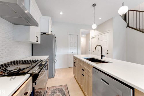 Modern kitchen featuring a white hexagonal tile backsplash, stainless steel appliances, a center island with a black sink, and light wood-finish cabinetry - 1263 Watt Drive Sw, Edmonton, AB - Indoor Photo Showing Kitchen With Double Sink With Upgraded Kitchen