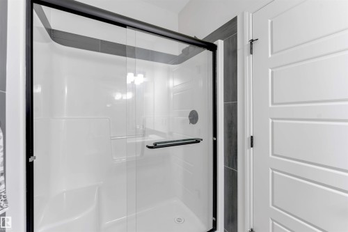 Enclosed shower with black-framed glass doors, integrated shelving, dark tile surround, and matte black hardware - 1263 Watt Drive Sw, Edmonton, AB - Indoor Photo Showing Bathroom