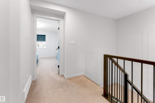 Carpeted hallway with a dark wood-finish and metal baluster railing, white trim, and a panel-style door - 1263 Watt Drive Sw, Edmonton, AB - Indoor Photo Showing Other Room