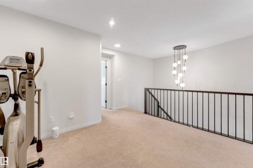 Spacious loft-style room featuring neutral carpet flooring, recessed ceiling lighting, and a modern black metal railing system - 1263 Watt Drive Sw, Edmonton, AB - Indoor