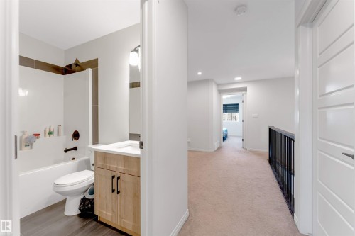 Contemporary bathroom with a white tub-shower combination, wood-finish vanity, and dark tile flooring - 1263 Watt Drive Sw, Edmonton, AB - Indoor Photo Showing Bathroom