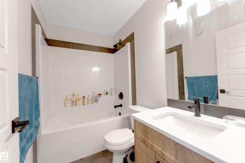 Bathroom featuring a built-in tub and shower combination, a wood-finish vanity with an integrated sink, a rectangular mirror, and dark-toned fixtures - 1263 Watt Drive Sw, Edmonton, AB - Indoor Photo Showing Bathroom
