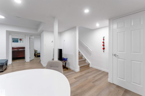 Recessed lighting illuminates wood-finish flooring throughout the space, featuring a staircase with a white handrail and a white paneled interior door - 1263 Watt Drive Sw, Edmonton, AB - Indoor Photo Showing Other Room