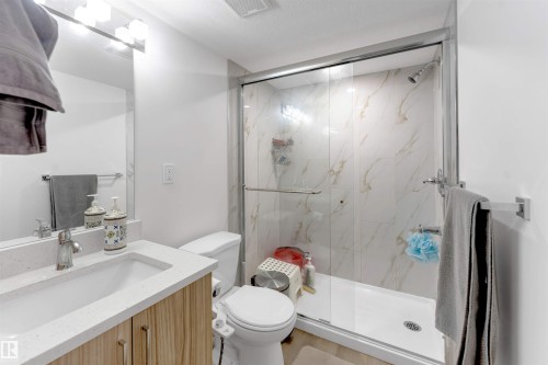 Bathroom featuring a single vanity with a white countertop, a shower enclosure with glass doors, and a white toilet - 1263 Watt Drive Sw, Edmonton, AB - Indoor Photo Showing Bathroom