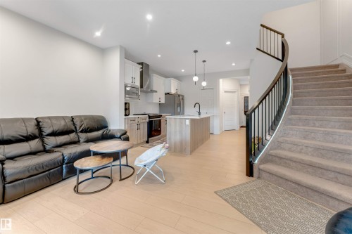 Open-concept living space with light wood-finish flooring, recessed lighting, a modern kitchen island, and a curved staircase with black metal balusters - 1263 Watt Drive Sw, Edmonton, AB - Indoor Photo Showing Living Room