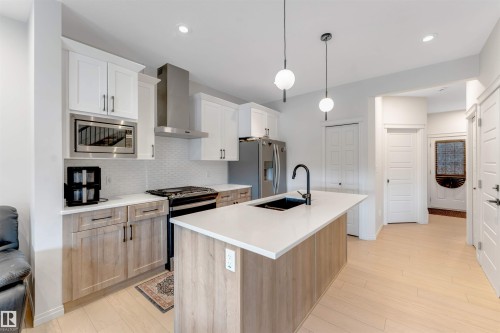 Kitchen featuring light wood-finish flooring, a central island with a solid surface countertop, white upper cabinetry, natural wood-finish lower cabinetry, and stainless steel appliances - 1263 Watt Drive Sw, Edmonton, AB - Indoor Photo Showing Kitchen With Upgraded Kitchen