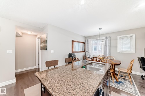 Kitchen island with a granite countertop and an integrated sink, wood-finish flooring, recessed ceiling lighting, and a modern circular pendant light fixture - #138 655 Tamarack Rd Nw, Edmonton, AB - Indoor