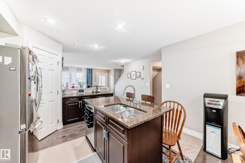 Kitchen featuring a central island with dual sinks, granite-finish countertops, stainless steel appliances, and wood-finish flooring - #138 655 Tamarack Rd Nw, Edmonton, AB - Indoor Photo Showing Other Room
