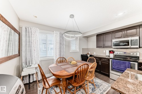 Dark wood-finish cabinetry, stainless steel range and microwave, wood-finish flooring, recessed lighting, and a modern chandelier - #138 655 Tamarack Rd Nw, Edmonton, AB - Indoor