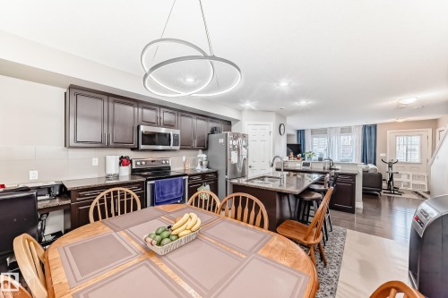 Kitchen featuring dark wood cabinetry, stainless steel appliances, a center island with bar seating, and recessed lighting - #138 655 Tamarack Rd Nw, Edmonton, AB - Indoor