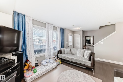 Recessed ceiling light, dark wood-finish flooring, multiple windows with blinds, white trim, and a white interior door - #138 655 Tamarack Rd Nw, Edmonton, AB - Indoor Photo Showing Living Room