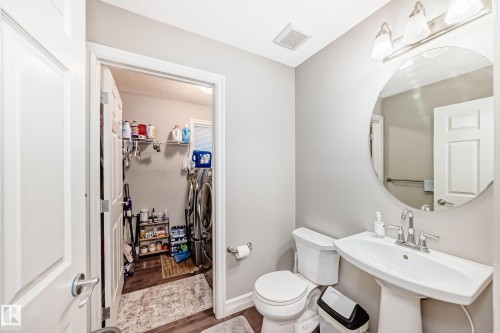 Pedestal sink with chrome faucet, circular mirror, and wall-mounted light fixture - #138 655 Tamarack Rd Nw, Edmonton, AB - Indoor Photo Showing Bathroom