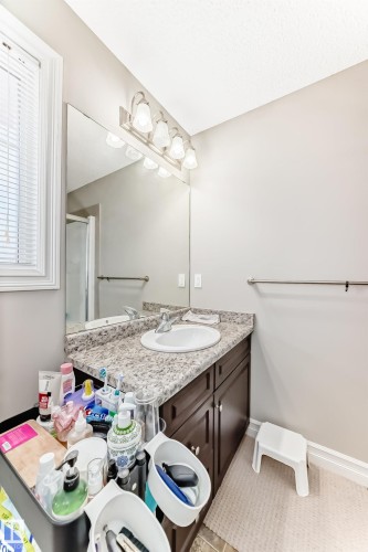 Vanity with a single basin sink, granite-style countertop, and dark wood-finish cabinetry - #138 655 Tamarack Rd Nw, Edmonton, AB - Indoor Photo Showing Bathroom