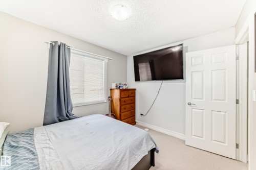 Wall-mounted television bracket, neutral wall paint, textured ceiling, window with blinds, panel interior door - #138 655 Tamarack Rd Nw, Edmonton, AB - Indoor Photo Showing Bedroom