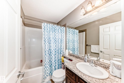 Bathroom featuring a white tub/shower combination, vanity with an oval undermount sink, speckled countertop, and a large wall-mounted mirror with overhead lighting - #138 655 Tamarack Rd Nw, Edmonton, AB - Indoor Photo Showing Bathroom