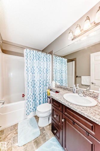 Built-in vanity with a single basin sink, speckled countertop, and dark wood-finish cabinetry - #138 655 Tamarack Rd Nw, Edmonton, AB - Indoor Photo Showing Bathroom