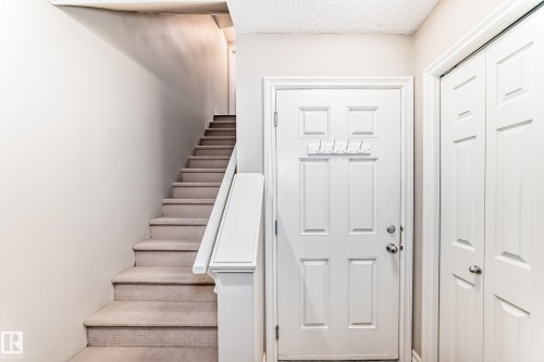 Carpeted staircase with white railing, paneled entry door, and bi-fold closet doors - #138 655 Tamarack Rd Nw, Edmonton, AB - Indoor Photo Showing Other Room