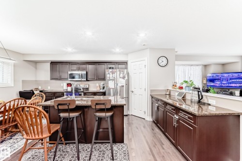 Kitchen featuring dark wood cabinetry, stainless steel appliances, granite countertops, and wood-finish flooring - #138 655 Tamarack Rd Nw, Edmonton, AB - Indoor Photo Showing Kitchen