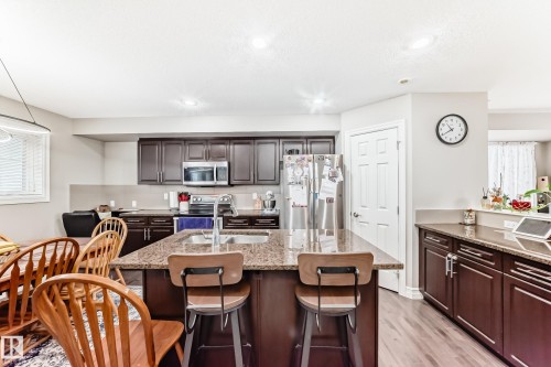 Kitchen featuring rich wood cabinetry, granite countertops, a stainless steel refrigerator, and a center island with sink - #138 655 Tamarack Rd Nw, Edmonton, AB - Indoor Photo Showing Other Room