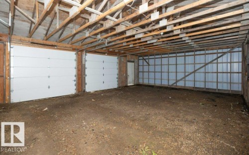 Spacious garage with exposed wood rafters, two white panel garage doors, and corrugated metal wall paneling - 26417 Twp Rd 582, Rural Westlock County, AB - Indoor Photo Showing Garage