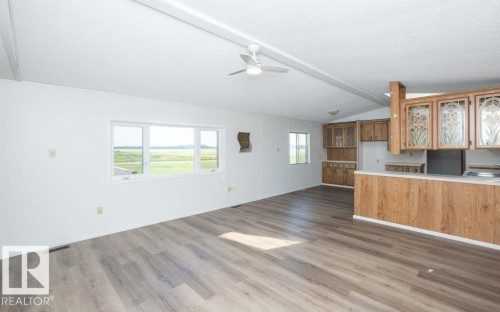 Wood-finish flooring, white walls, multiple windows, ceiling fan, and wood cabinetry with decorative glass inserts - 26417 Twp Rd 582, Rural Westlock County, AB - Indoor Photo Showing Kitchen