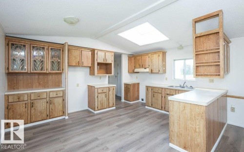 Kitchen featuring a skylight, ample wood-finish cabinetry, a double basin sink, and wood-finish flooring - 26417 Twp Rd 582, Rural Westlock County, AB - Indoor Photo Showing Kitchen With Double Sink