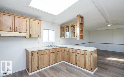 Bright kitchen featuring natural skylight illumination, L-shaped wood cabinetry with ample storage, white countertops, and wood-finish flooring throughout - 26417 Twp Rd 582, Rural Westlock County, AB - Indoor Photo Showing Kitchen With Double Sink