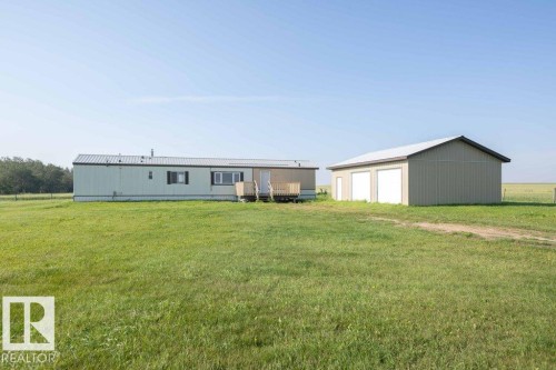 Expansive green field featuring a light-sided residence with a metal roof and a separate multi-bay garage structure - 26417 Twp Rd 582, Rural Westlock County, AB - Outdoor