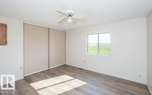 Wood-finish flooring with a ceiling fan, sliding closet doors, and a window framing an expansive outdoor landscape - 26417 Twp Rd 582, Rural Westlock County, AB - Indoor Photo Showing Other Room