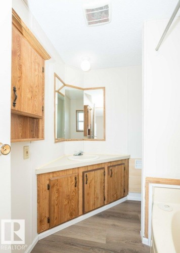 Corner vanity with a built-in sink, wood-finish cabinetry, wood-finish flooring, and a mirrored wall - 26417 Twp Rd 582, Rural Westlock County, AB - Indoor Photo Showing Bathroom