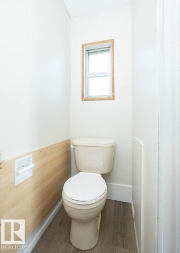 Compact powder room featuring a one-piece toilet with elongated bowl, wood-finish wainscoting, and a wood-framed window with operable shutters for natural light and ventilation - 26417 Twp Rd 582, Rural Westlock County, AB - Indoor Photo Showing Bathroom