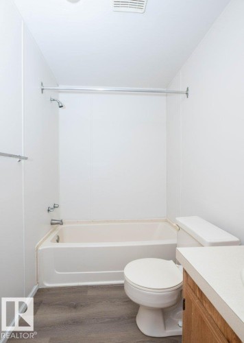 Tub and shower combination with chrome fixtures, toilet, vanity with solid surface countertop, and wood-finish flooring - 26417 Twp Rd 582, Rural Westlock County, AB - Indoor Photo Showing Bathroom