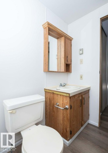 Compact bathroom featuring a wood-finish vanity with an integrated sink, coordinating wood-finish medicine cabinet, and light-toned flooring - 26417 Twp Rd 582, Rural Westlock County, AB - Indoor Photo Showing Bathroom